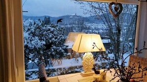 Une pièce avec vue sur un paysage enneigé, visible à travers une fenêtre, une lampe sur une table et un objet décoratif en forme de cœur.