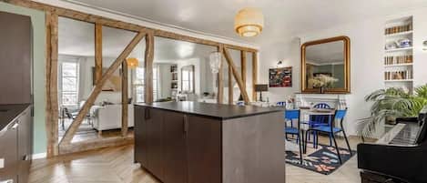 A modern kitchen with a central island, wooden beams, and a dining area with blue chairs.