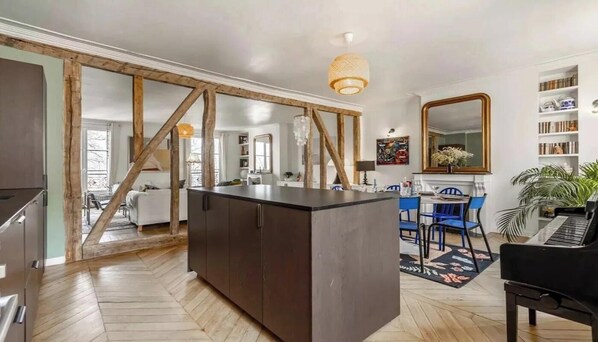 A modern kitchen with a central island, wooden beams, and a dining area with blue chairs.