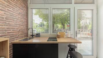 A kitchen with a brick wall, a wooden countertop, a sink, and a window with blinds.