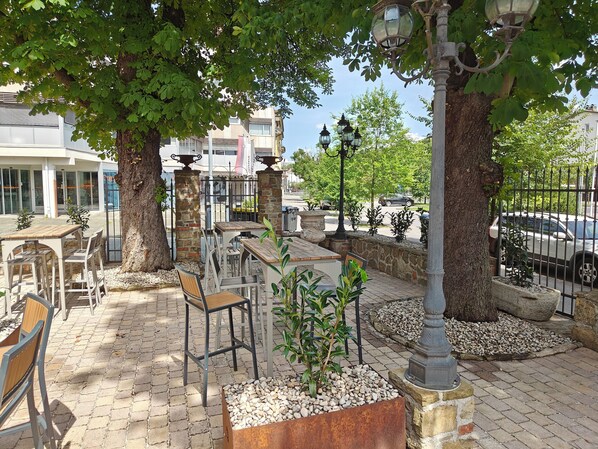 An outdoor seating area with tables and chairs, surrounded by trees and a stone wall. - Aroma Apartments (Ljubljana)