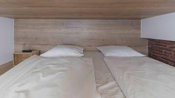 A double bed with white linens in a room with a wooden ceiling and a brick wall.