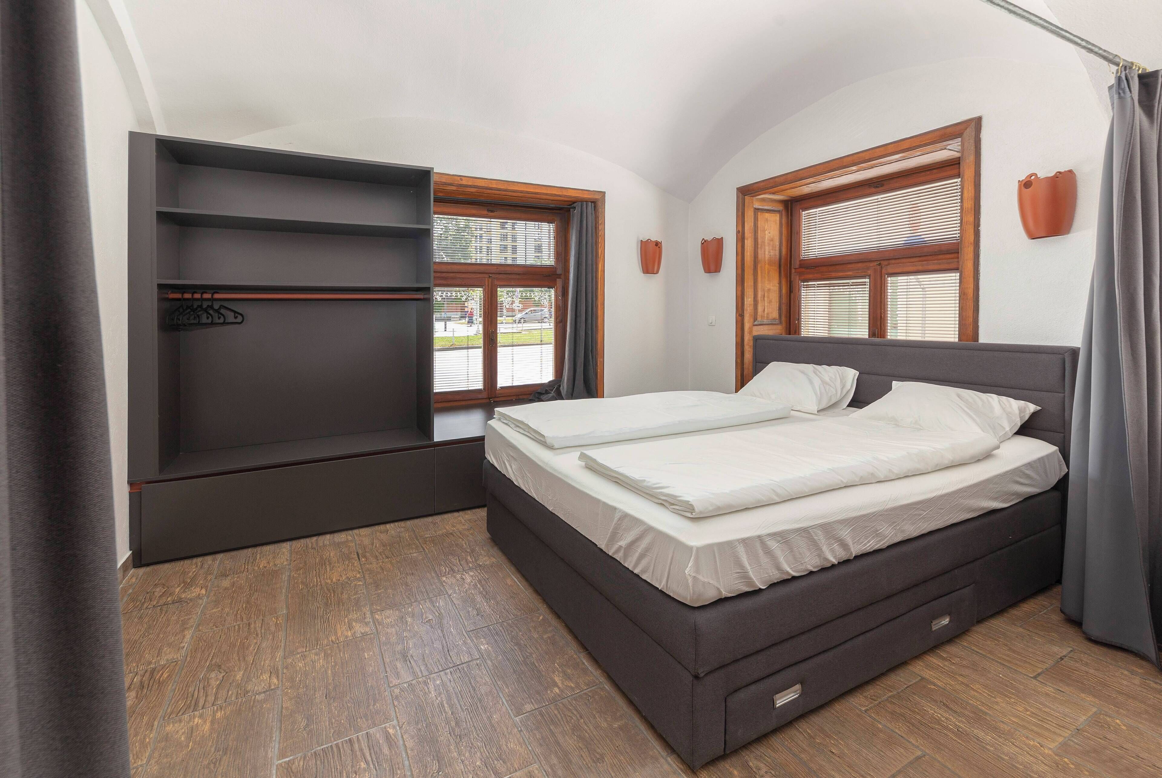 Ein Schlafzimmer mit einem Bett, Einbauschränken und zwei Fenstern mit Jalousien.