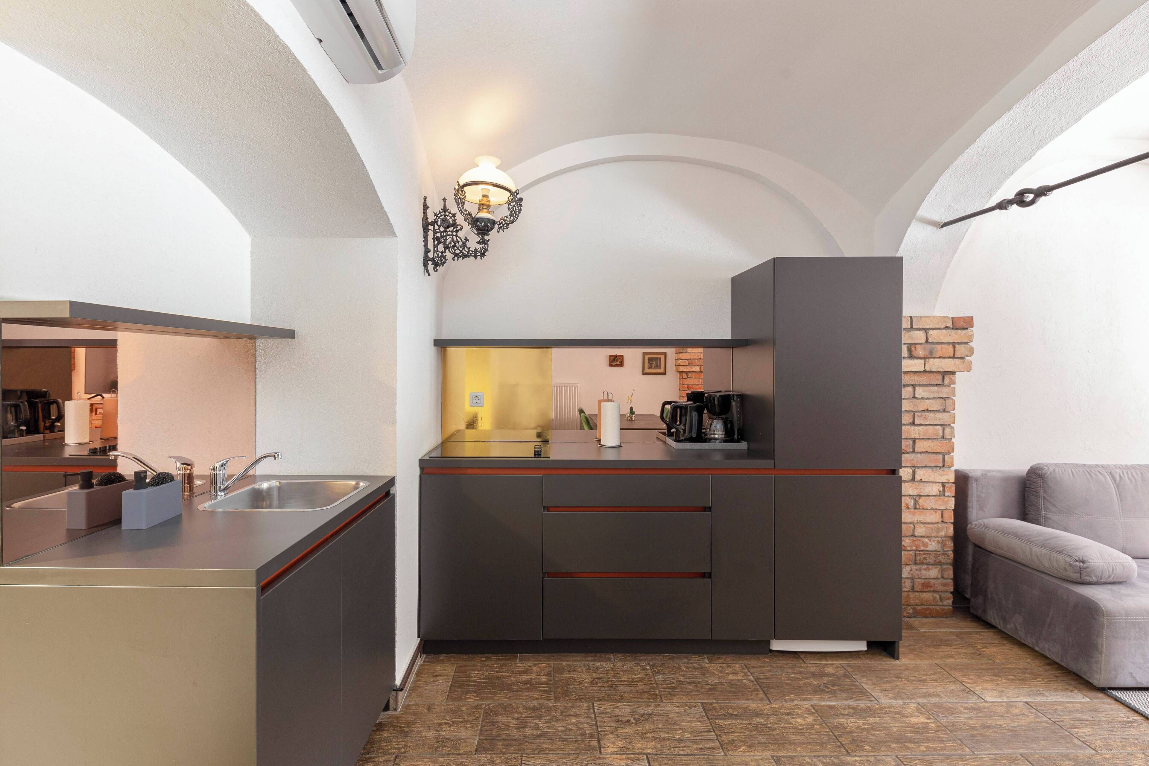 A compact kitchen with a modern design, featuring a built-in sink, a coffee machine, and a brick accent wall.