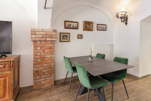 Un área de comedor con pared de ladrillo, sillas verdes, una mesa oscura y cuadros en la pared.