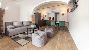 Un soggiorno moderno con un divano, un tavolino da caffè e pouf. Si nota una cucina sullo sfondo con un'area pranzo.