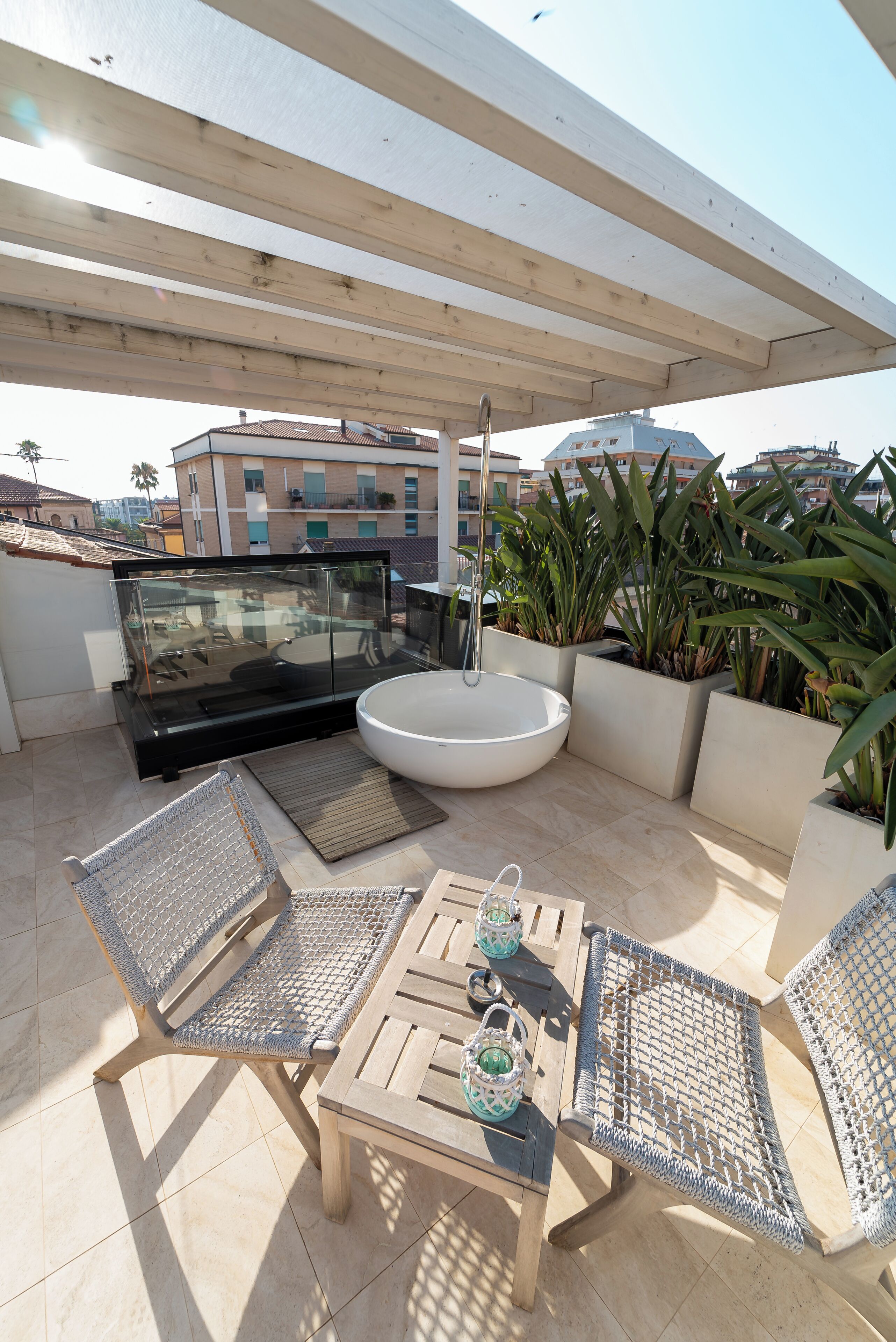 A rooftop terrace with a glass balustrade, outdoor seating, and potted plants.