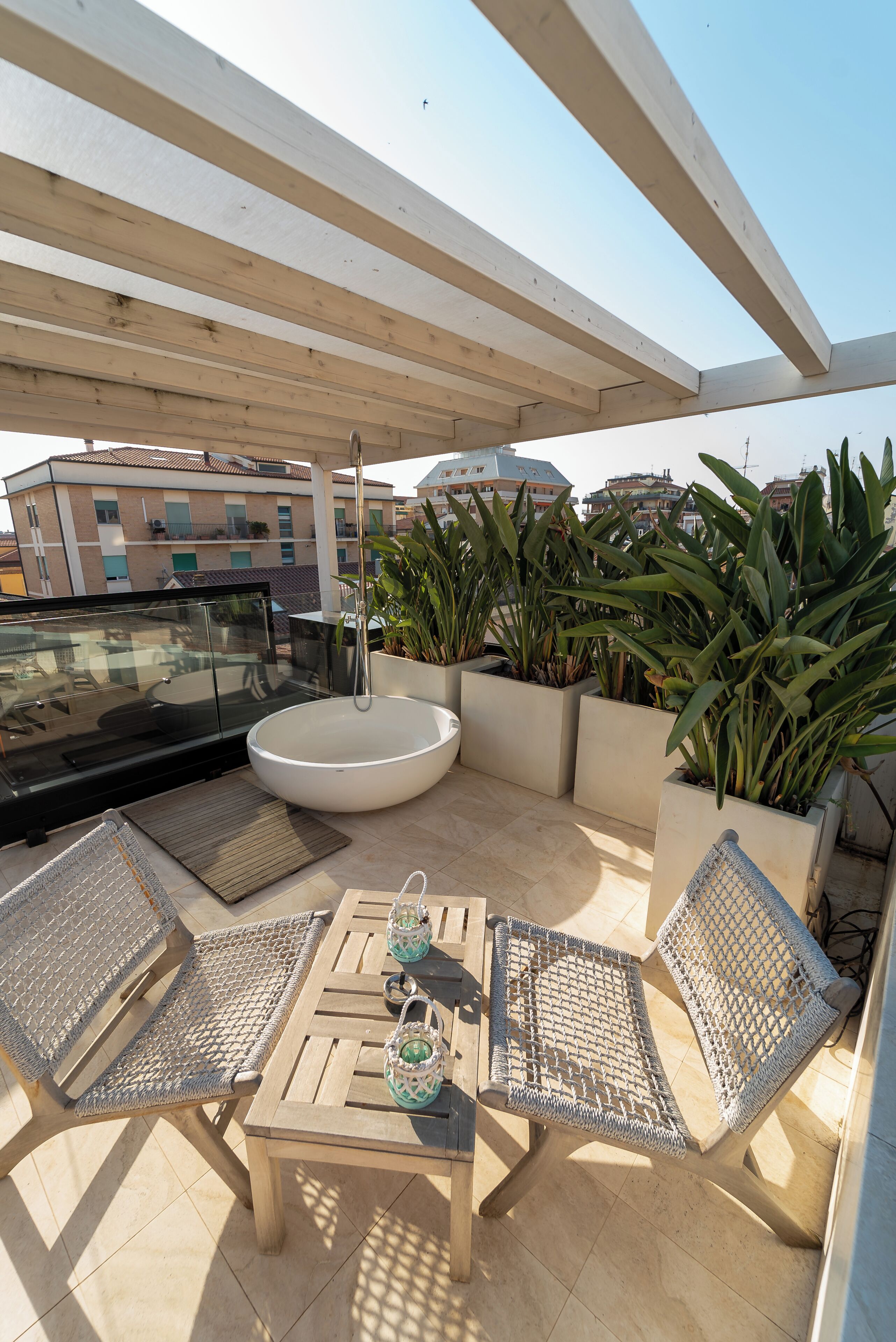 A rooftop terrace with a dining table, chairs, a large planter with plants, and a hanging light fixture.