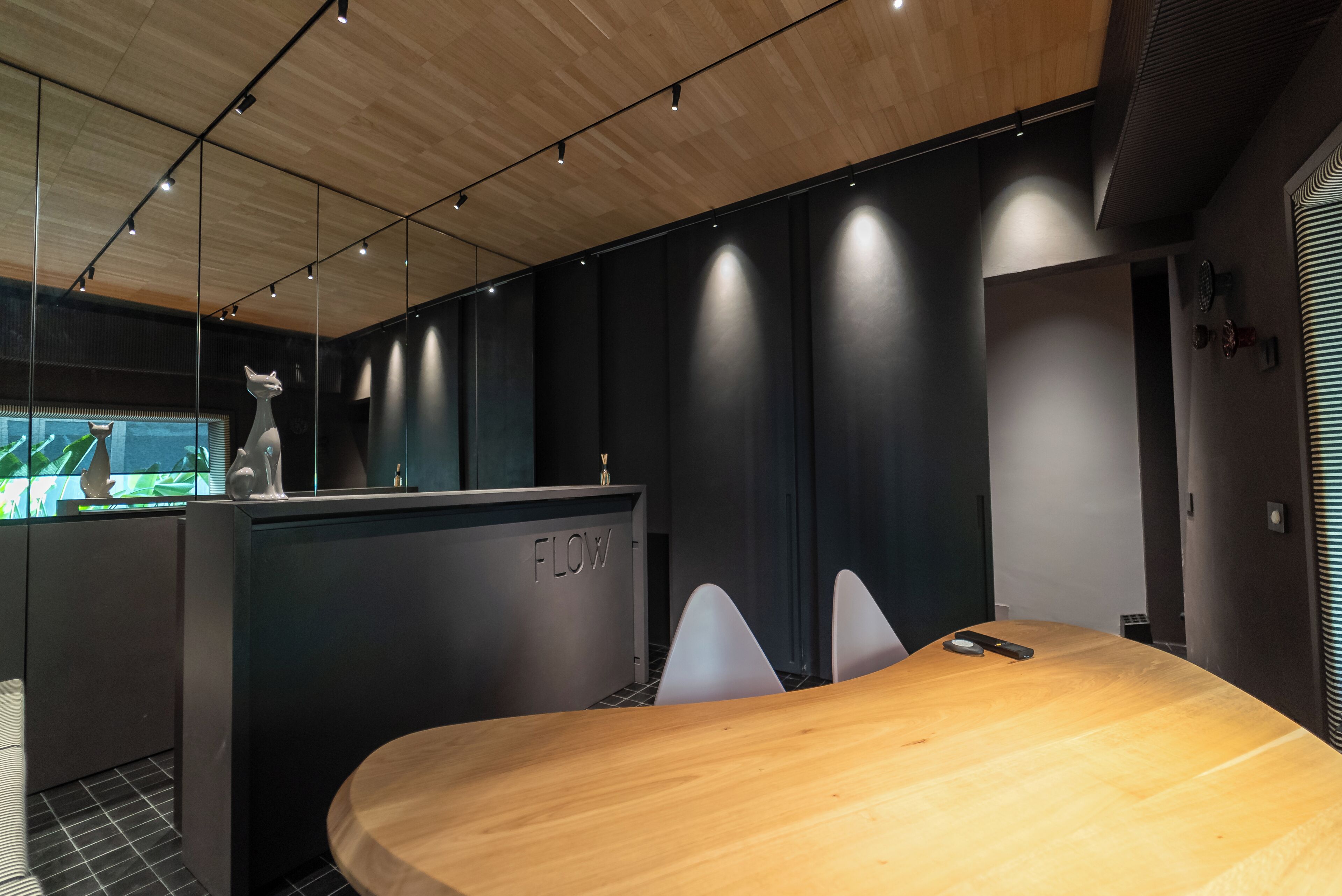 A modern conference room with a wooden table, two white chairs, and a reception desk labeled "FLOW".