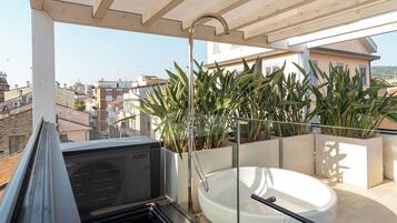 Un balcón con bañera integrada, plantas en macetas y vista a la ciudad.