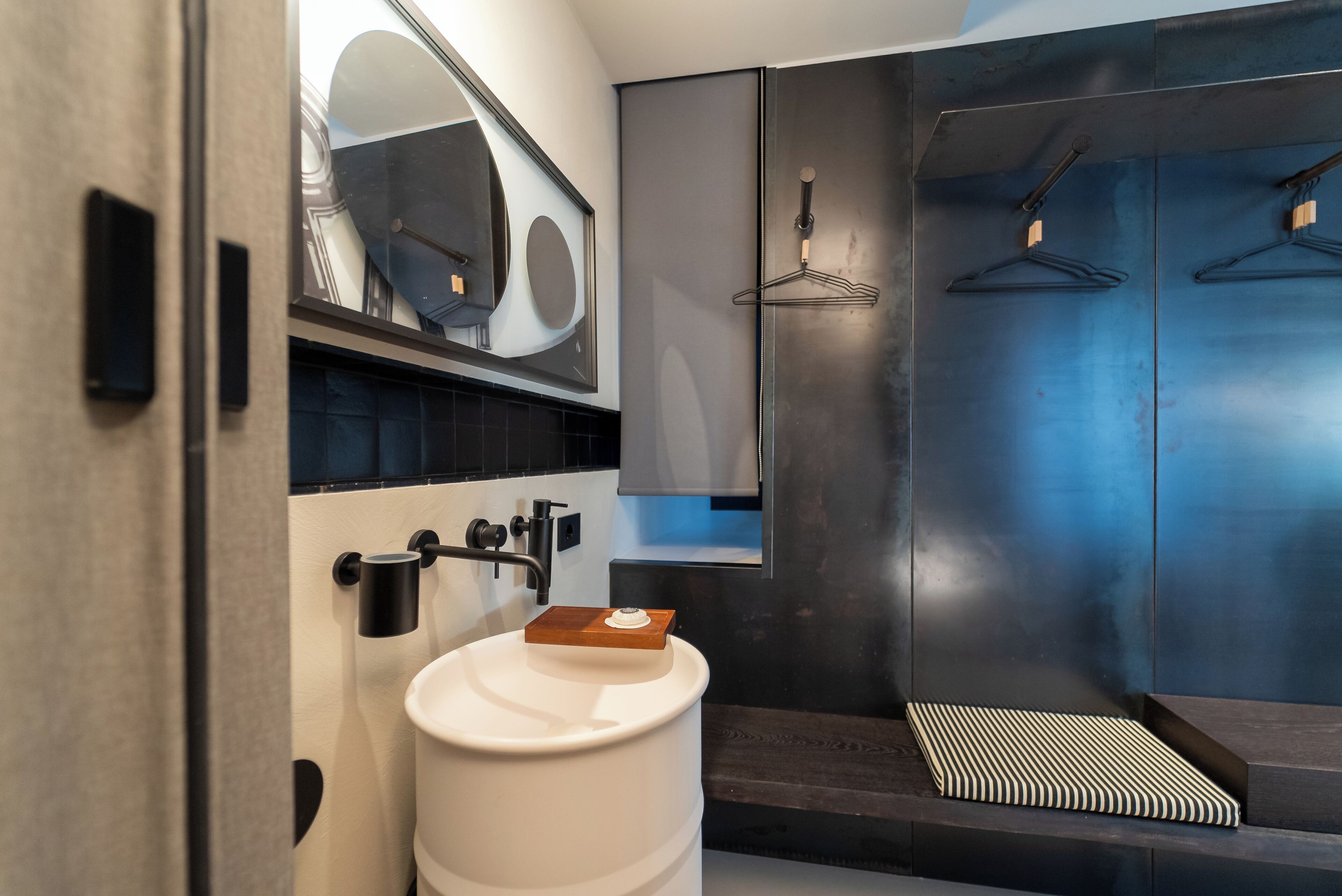 A modern bathroom with a large mirror, a white sink, and a shower area with a black and white striped bath mat.