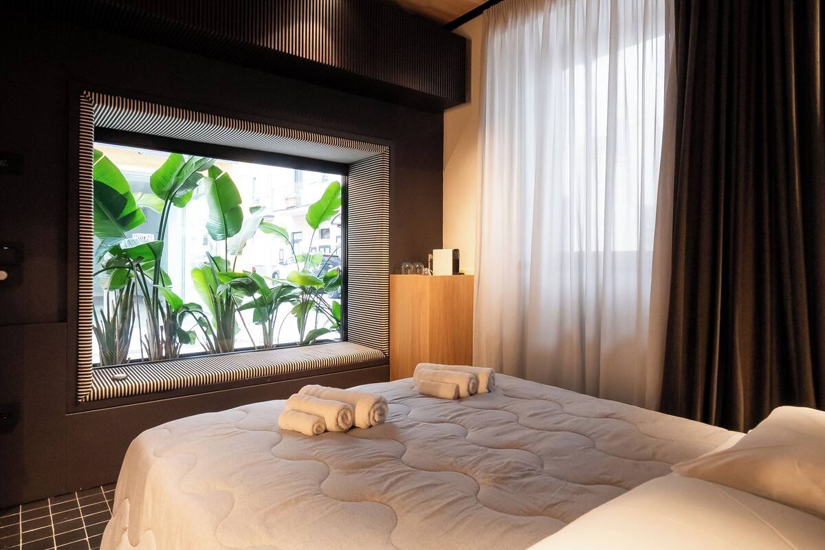 Una habitación de hotel moderna con una cama grande, un ventanal con vistas a zonas verdes y techo de madera.