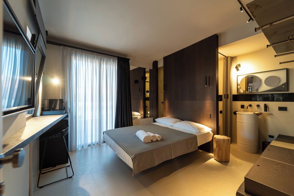 Habitación de hotel moderna con una cama grande, un escritorio, un tocador con espejo y un amplio ventanal con cortinas.