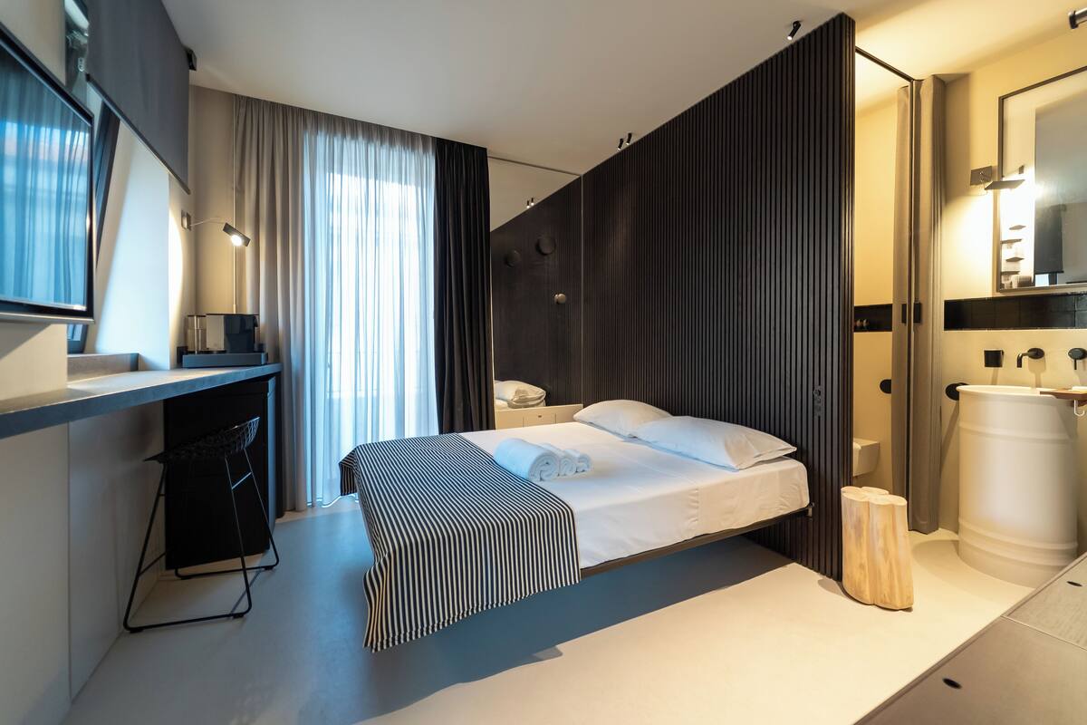 Una habitación de hotel moderna con una cama, un escritorio, una silla, un espejo grande y una ventana con cortinas.