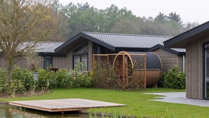 A modern building with a wooden deck over a pond, surrounded by greenery. - Eco Villa in Latour With Garden Sauna (Oirschot)