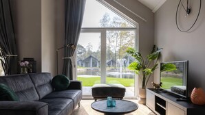 A modern living room with a leather sofa, a round coffee table, and a TV on a wooden stand. - Eco Villa in Latour With Garden Sauna (Oirschot)