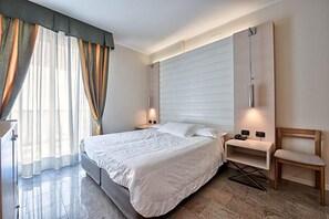 A modern hotel room with a large bed, a bedside table, a chair, and a wall-mounted TV. - Hotel Columbus (Lignano Sabbiadoro)