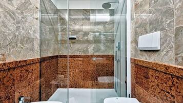 Ein modernes Badezimmer mit einer gläsernen Duschkabine, zwei Waschbecken und einer Wand aus Marmorfliesen.