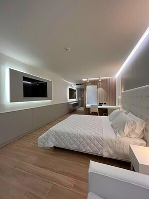 Un dormitorio moderno con una cama grande, un escritorio y un televisor en la pared.