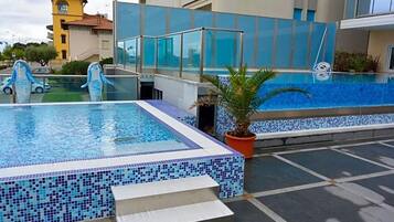 Ein Pool auf dem Dach mit klarem, blauem Wasser, umgeben von modernen Gebäuden und einer Palme.