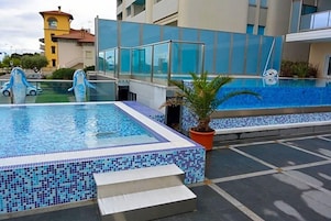 Una piscina sul tetto con acqua cristallina, circondata da edifici moderni e una palma.