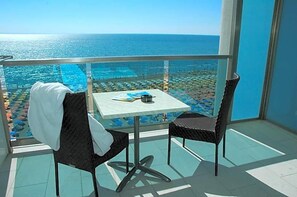 A balcony with a table and chairs, overlooking a pool and beach area. - Hotel Columbus (Lignano Sabbiadoro)
