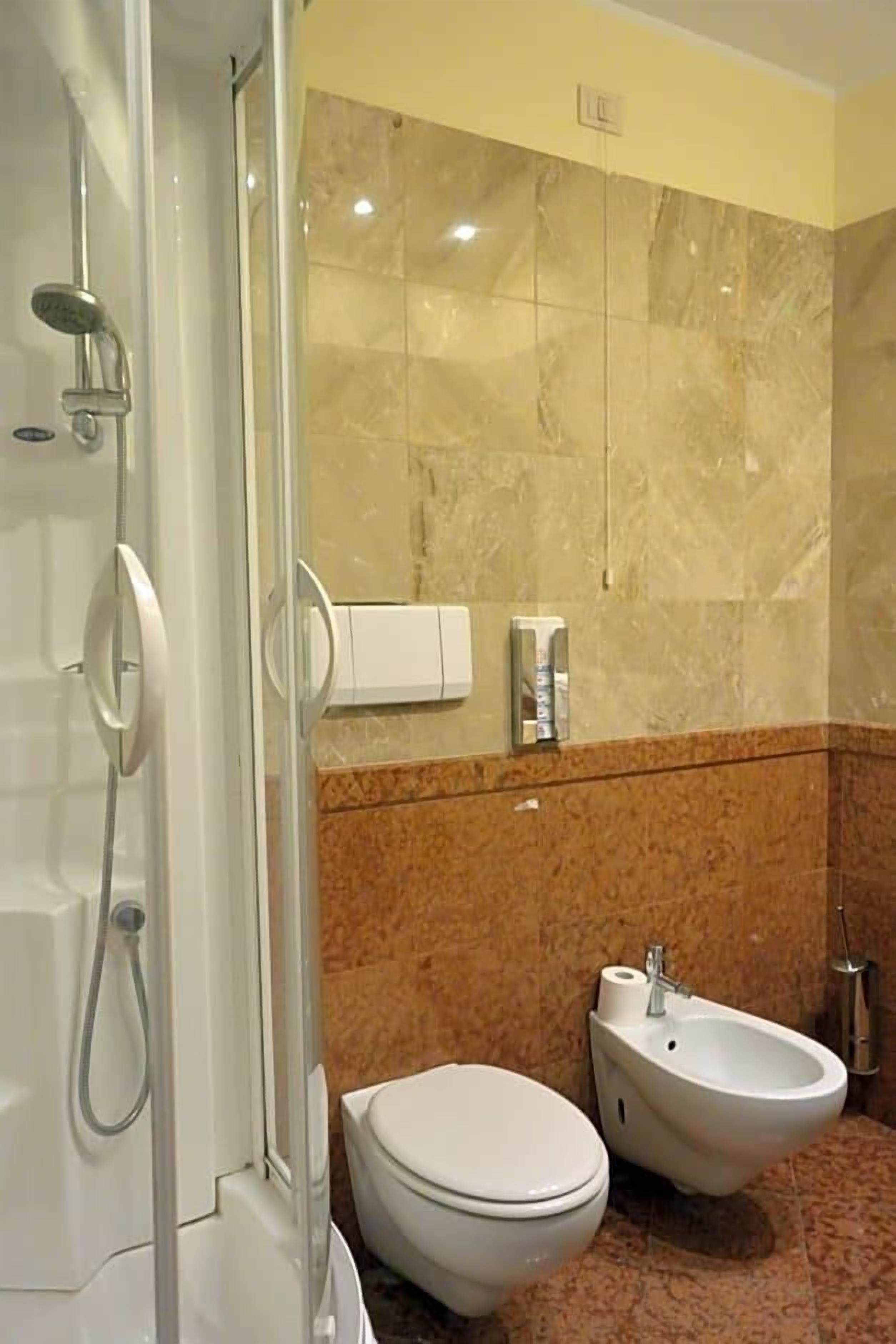 Een badkamer met douche, toilet, bidet en marmeren wanden.