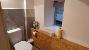 Et lille badeværelse med toilet, trækommode og et lille vindue.