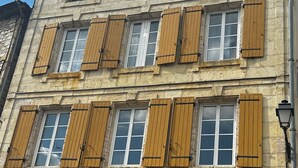 Un edifici amb diverses finestres, algunes amb persianes de fusta, i façana de pedra.