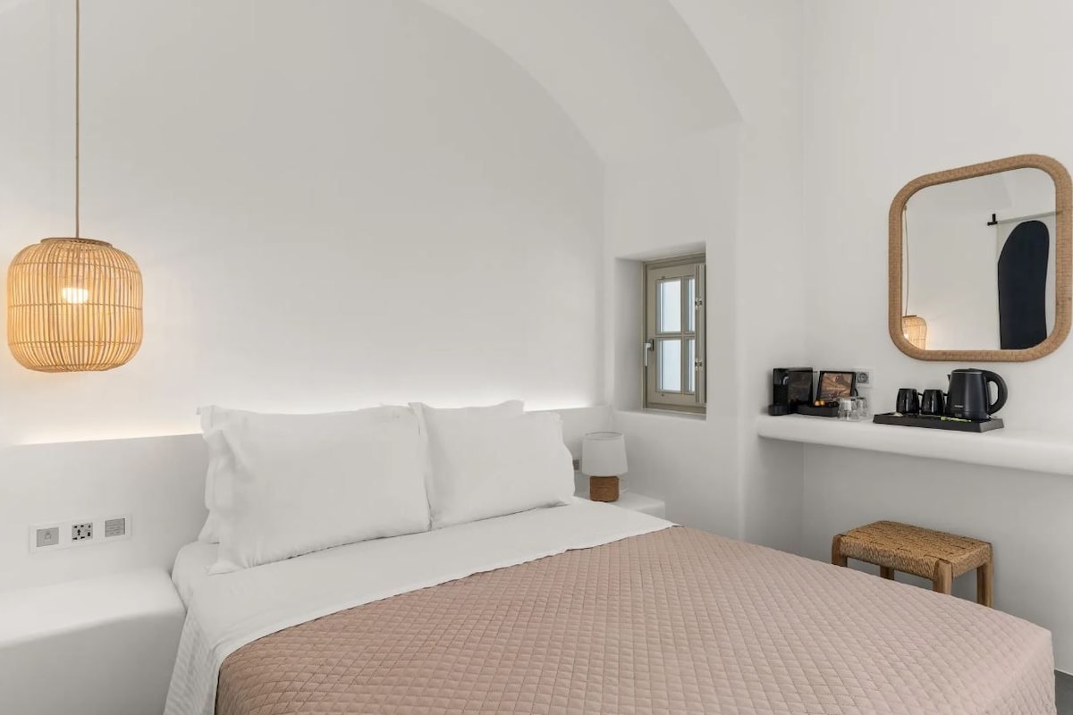 A minimalist bedroom with a bed, bedside table, lamp, and a small stool.