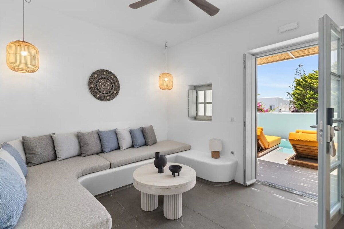 Una sala de estar moderna con un sofá modular, una mesa de centro redonda y una puerta de vidrio que da a una zona de estar exterior.