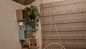 A cozy living room with a hanging chair, wooden shelves, a potted plant, and a patterned wall.