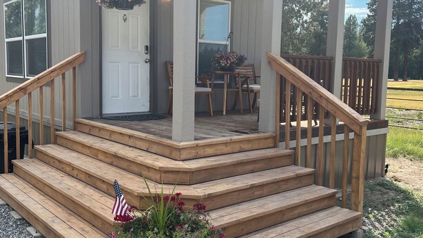 A wooden deck with a white door, a small porch, and a flag. - Cozy home on Cattle Ranch, close drive to Crater Lake National Park entrance.  (Chiloquin)