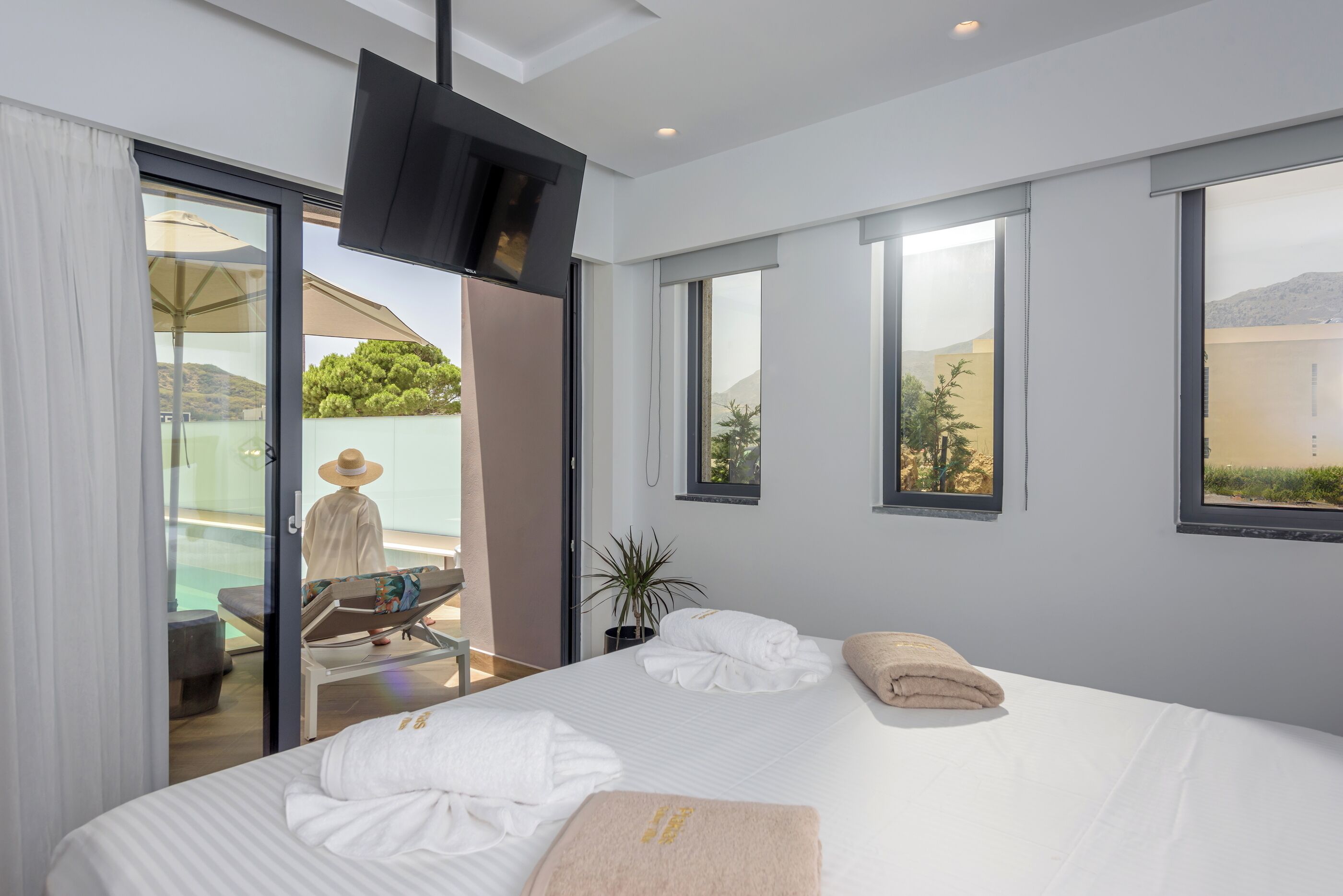 Een moderne hotelkamer met een groot bed, een aan de muur bevestigde televisie en een balkon met uitzicht op het landschap.