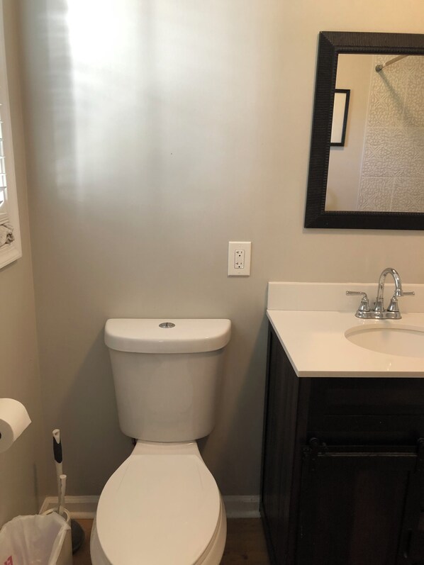 A bathroom with a white toilet, a sink with a mirror above it, and a wall socket.