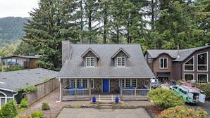 Une maison à deux étages avec un porche à l’avant, une allée et un véhicule garé dans l’allée.