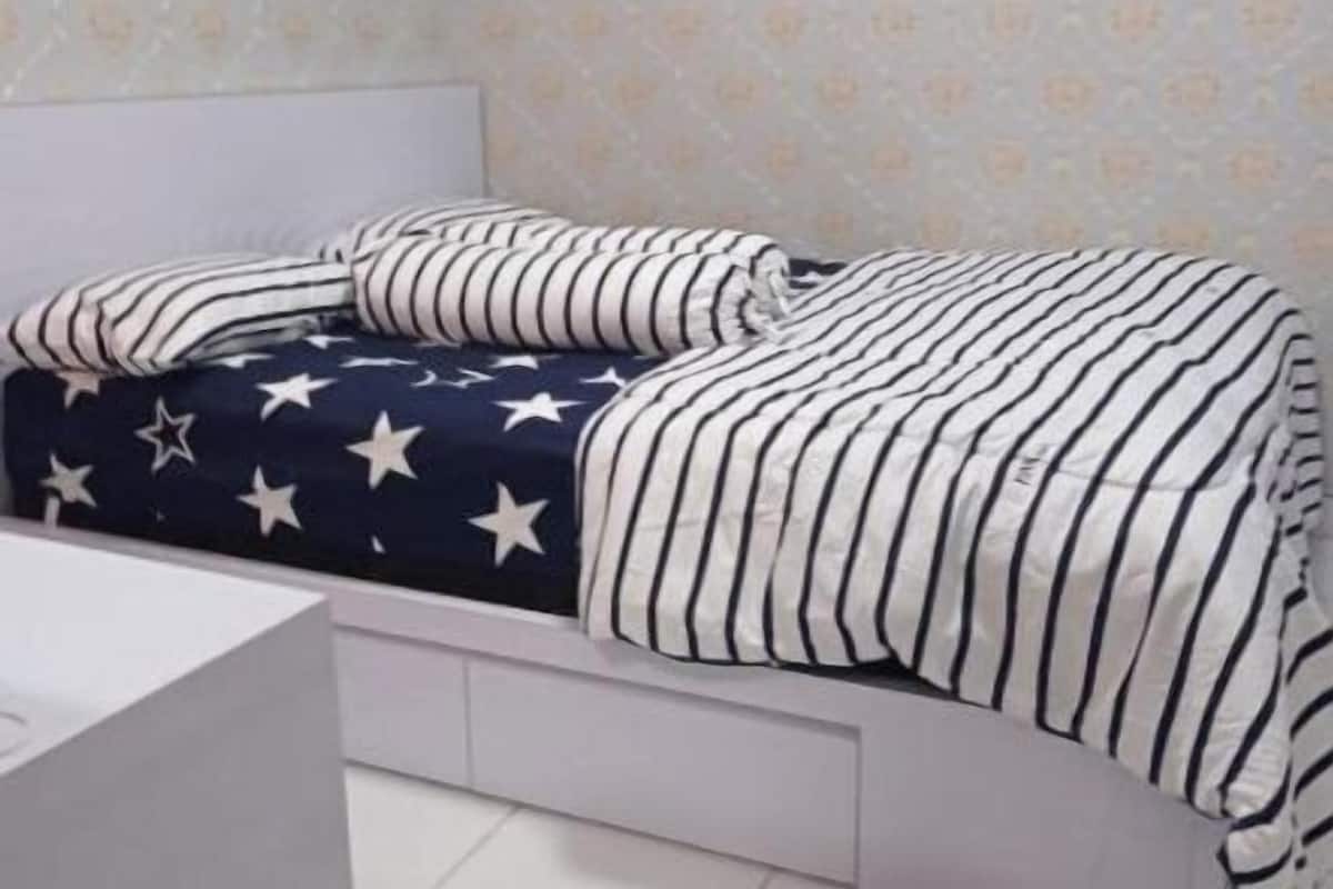 Ein Schlafzimmer mit einem Bett, das mit gestreifter Bettwäsche bezogen ist, einem Nachttisch und einer Wand mit Muster-Tapete.