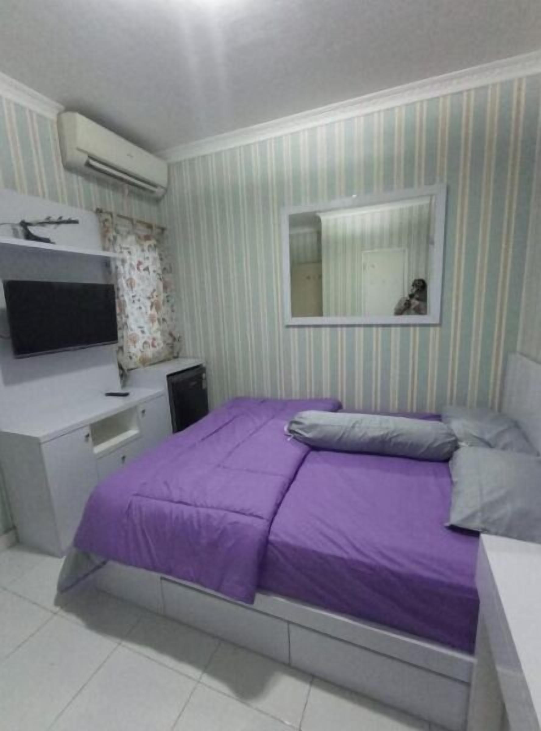 A bedroom with a bed, a TV, a desk, and a mirror.