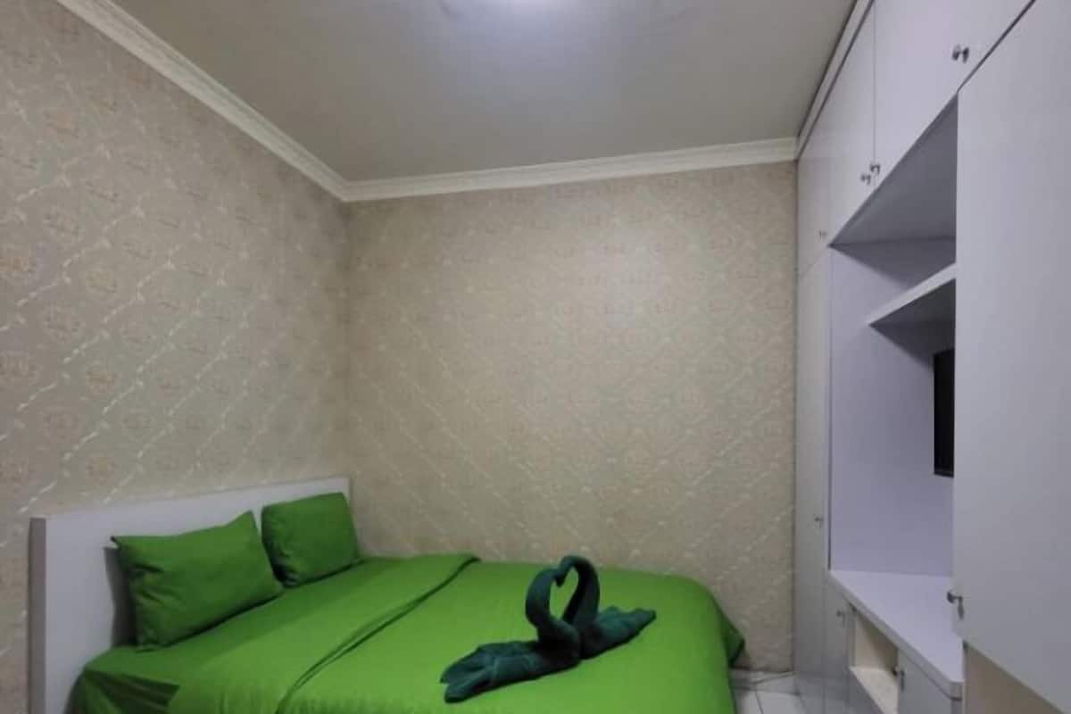 A bedroom with a bed, green bedding, a white headboard, a wardrobe, and a ceiling light.