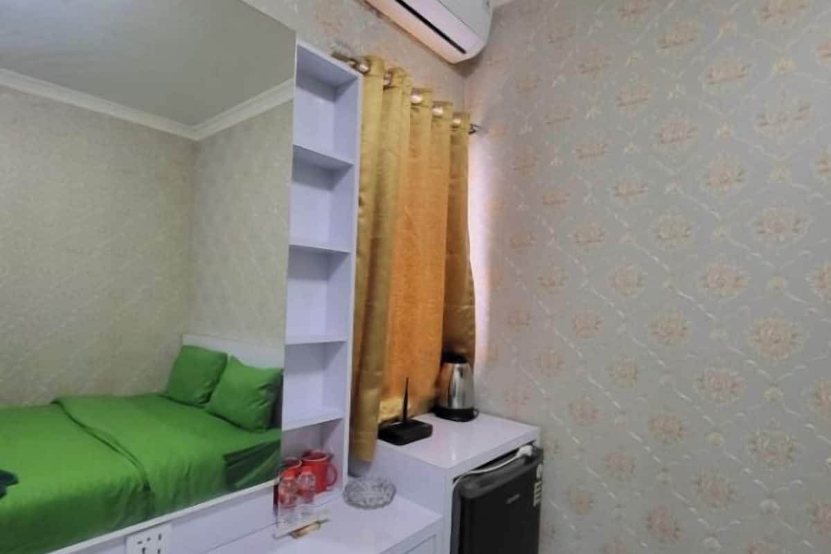 A small room with a bed, a desk, a chair, and an air conditioning unit.