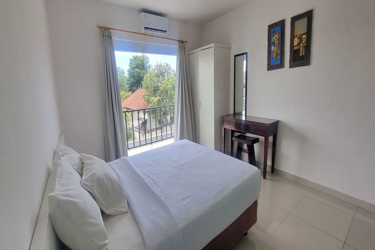 Un dormitorio con cama, escritorio, espejo y vistas al exterior.