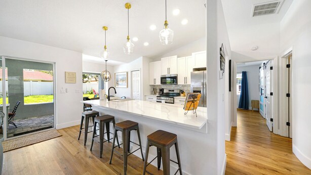 Una cocina moderna con una isla central, taburetes de bar, electrodomésticos de acero inoxidable e iluminación colgante.