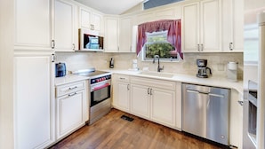 A kitchen with white cabinets, a built-in oven, a dishwasher, and a window with a curtain.