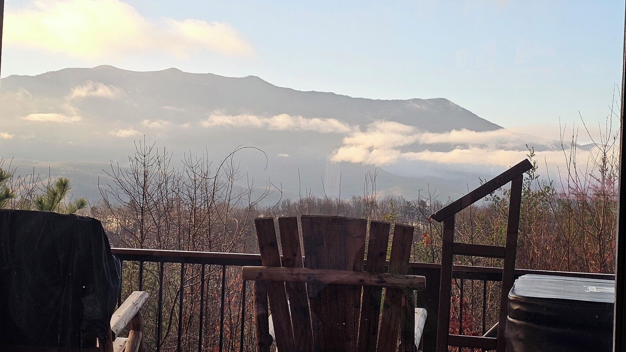 A wooden deck with a chair, overlooking a mountainous landscape with clouds.