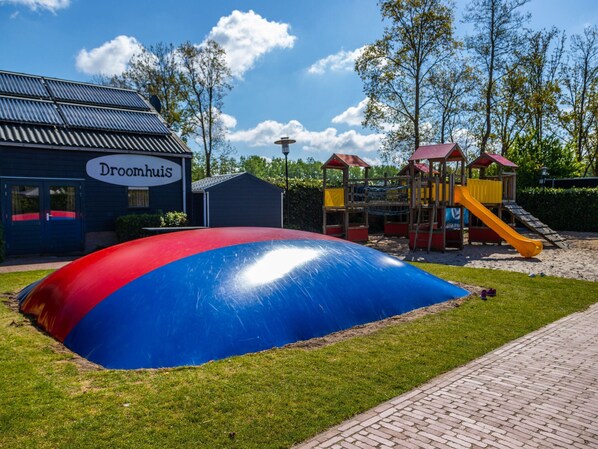 A playground with a large inflatable slide, a playhouse, and a building labeled "Droomhuis".