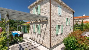 A stone building with green shutters, a covered patio, and a pool.