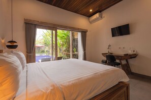 Habitación de hotel con cama, escritorio, silla, televisión y vista a una piscina y follaje.
