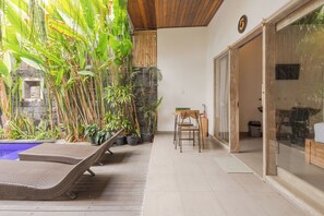 Een kamer met een houten plafond, een stenen muur, een glazen deur en een kleine tafel met stoelen.