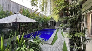 Una piscina rodeada de exuberante vegetación y una pérgola de madera.