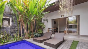 Un área de piscina con sillones de descanso, un muro de piedra y plantas tropicales.